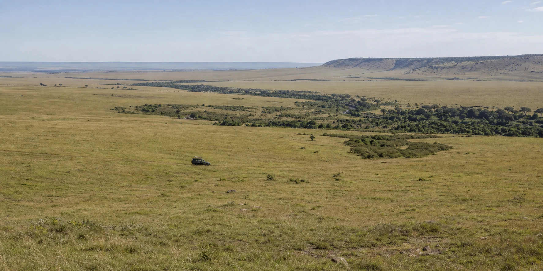 A small safari vehicle crossing broad grassland beneath a distant escarpment